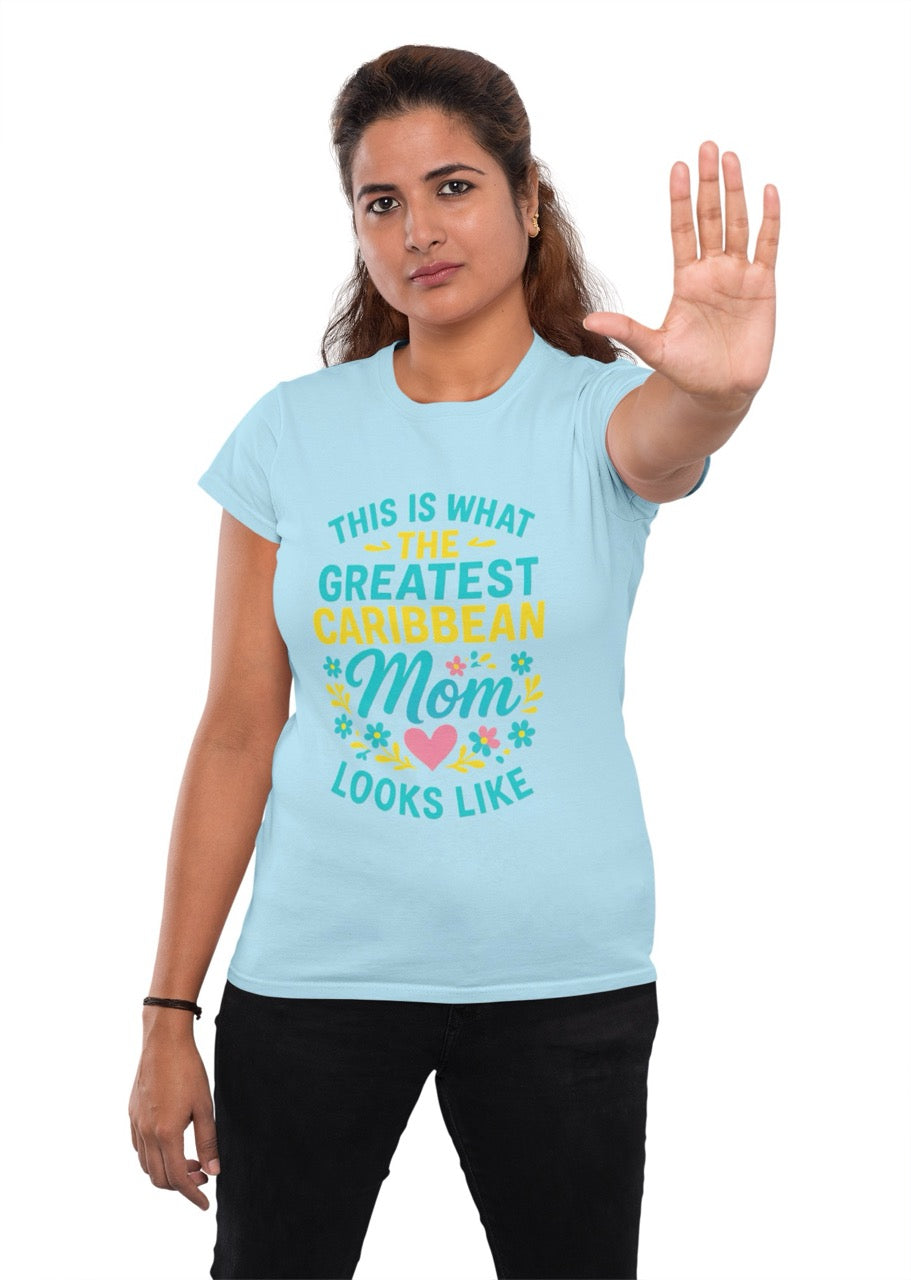 Woman wearing a blue T-shirt with colorful text reading “This is what the greatest Caribbean mom looks like,” decorated with flowers and a heart, raising her hand in a stop gesture.