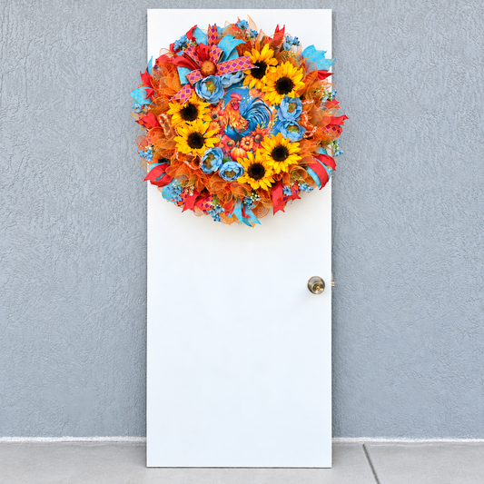 Handmade fall rooster wreath featuring vibrant yellow sunflowers, dusty blue flowers, orange deco mesh, coral and turquoise ribbons, and a colorful rooster centerpiece. A full farmhouse-style autumn wreath displayed on a white front door.