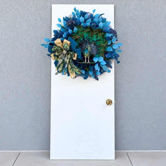 Full view of blue and teal peacock wreath with decorative berries and layered foliage.