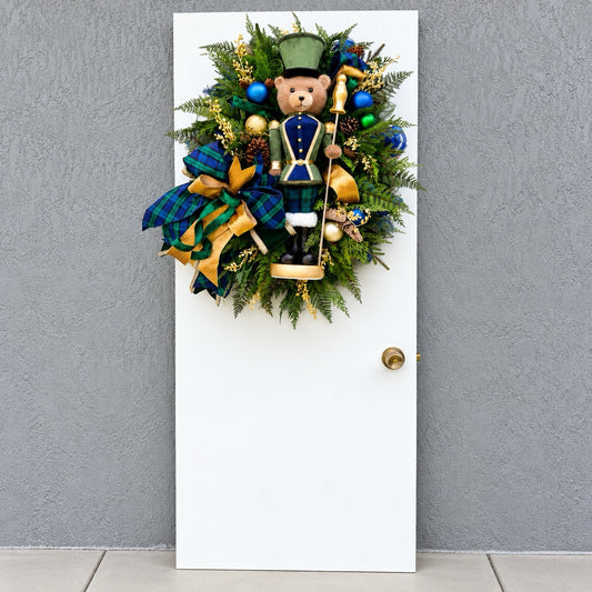 Full view of handmade teddy bear Christmas wreath with evergreen, navy ornaments and gold ribbon.