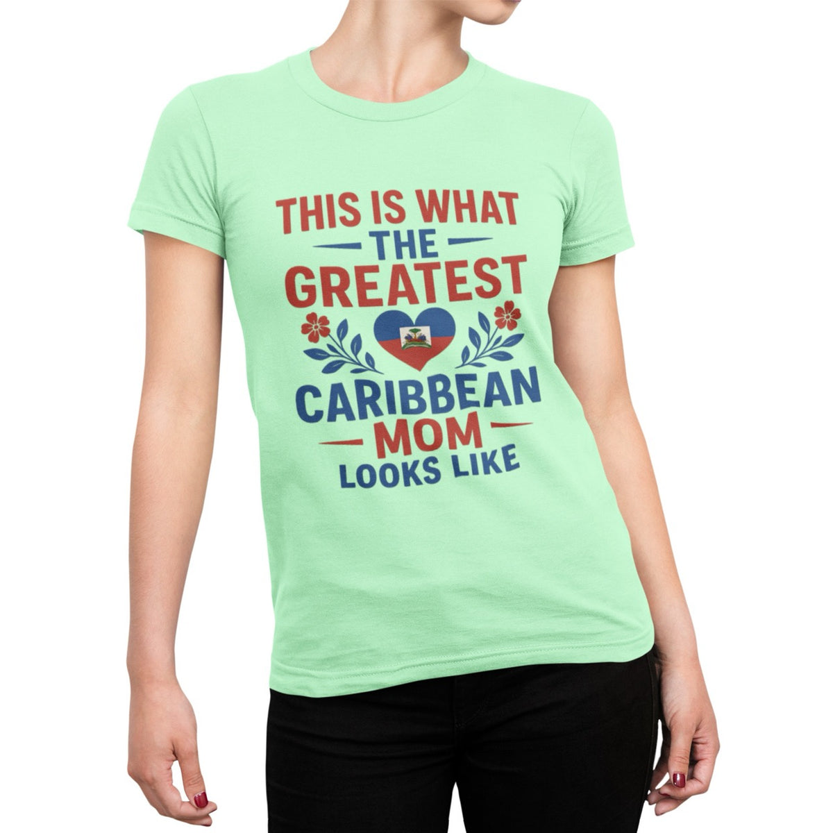 Woman wearing a pink T-shirt with bold red and blue text reading “This is what the greatest Caribbean mom looks like,” featuring a heart with the Haitian flag and floral accents.