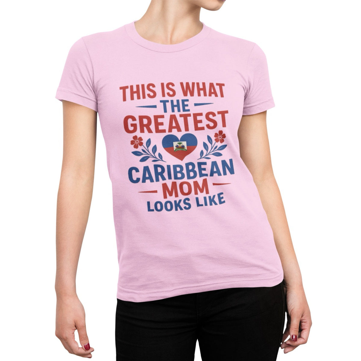 Woman wearing a pink T-shirt with bold red and blue text reading “This is what the greatest Caribbean mom looks like,” featuring a heart with the Haitian flag and floral accents.