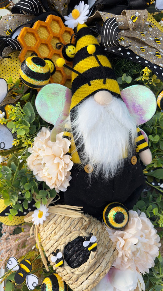 Luxury bee-themed door swag featuring a whimsical bee gnome, honeycomb decoration, beehive accent, premium black and yellow ribbons, lush greenery, cream florals, and sparkling bee embellishments, perfect for spring and summer front door décor.