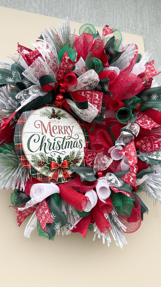Traditional plaid and pine Merry Christmas wreath with red, green and white ribbon, decorative mesh, frosted greenery and Christmas sign on a front door