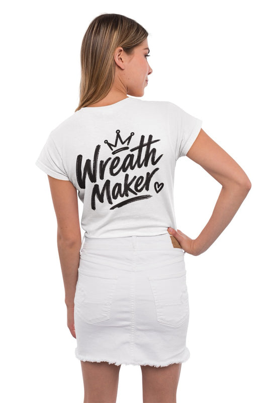 Back view of a t-shirt displaying the words “Wreath Maker” in large brush-style lettering with a crown above and a small heart beside the design. The shirt is available in various colors.