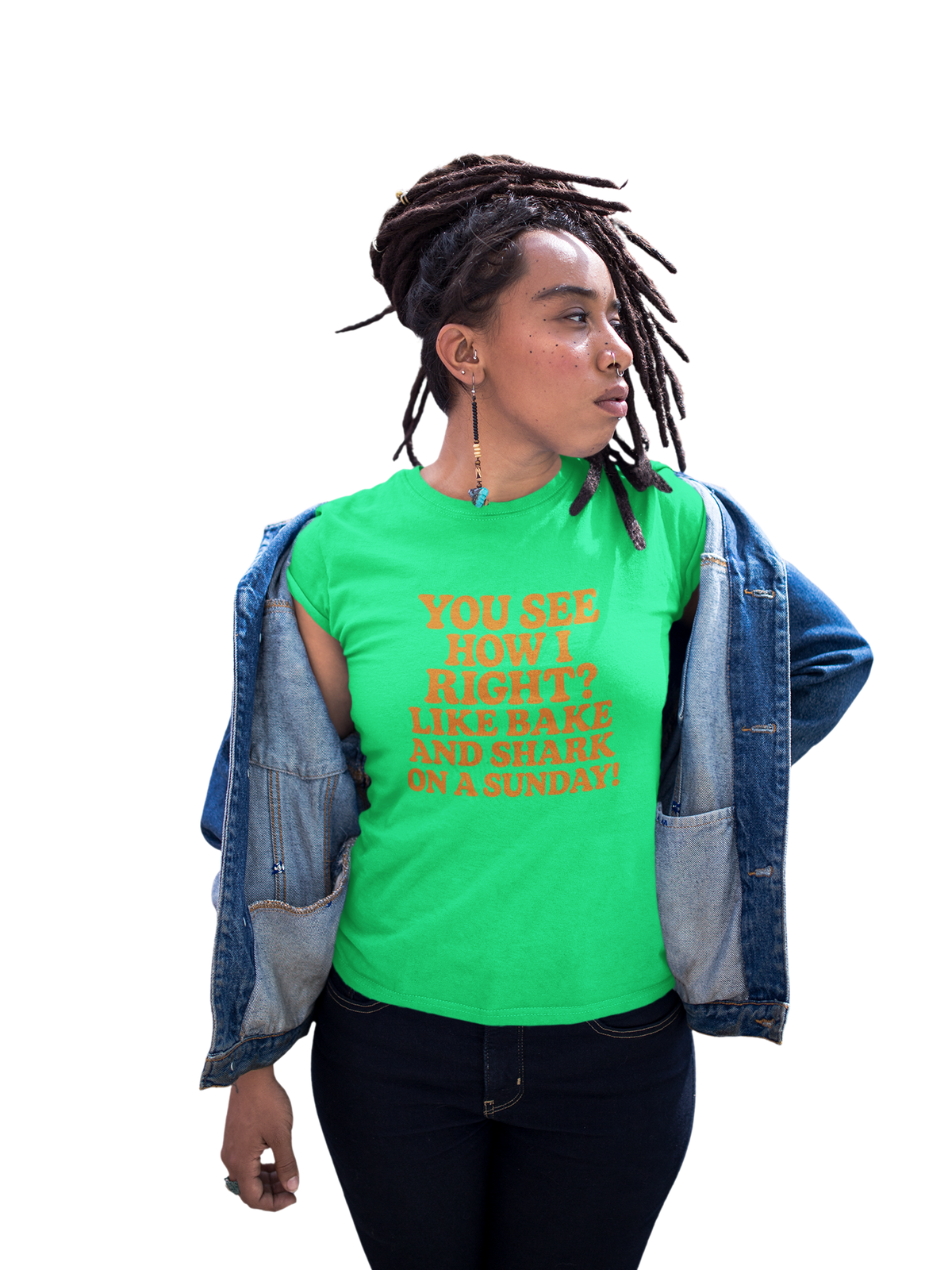 Woman wearing a light pink T-shirt with orange text reading “You see how I right? Like bake and shark on a Sunday!” and an open denim jacket against a white background.