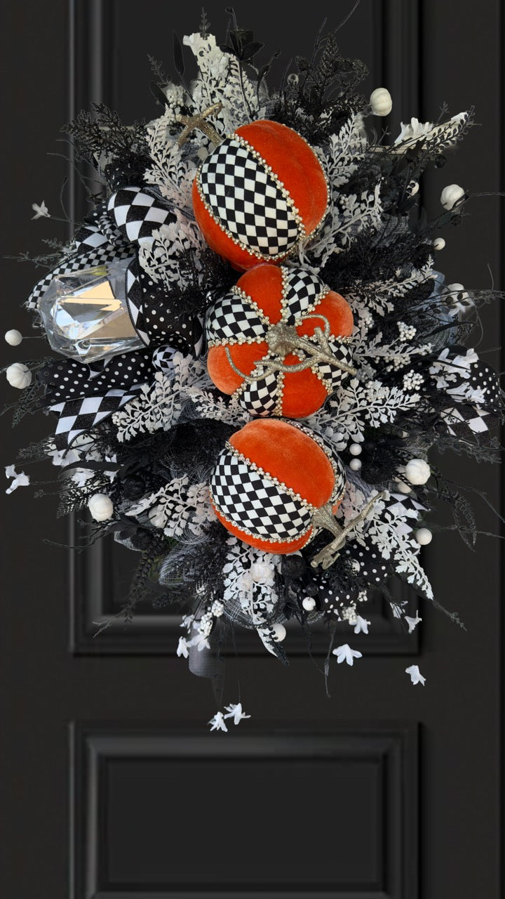 Handmade fall wreath with black‑and‑white checkered pumpkins, gold stems, and black, white, and silver foliage with patterned ribbons on a dark door