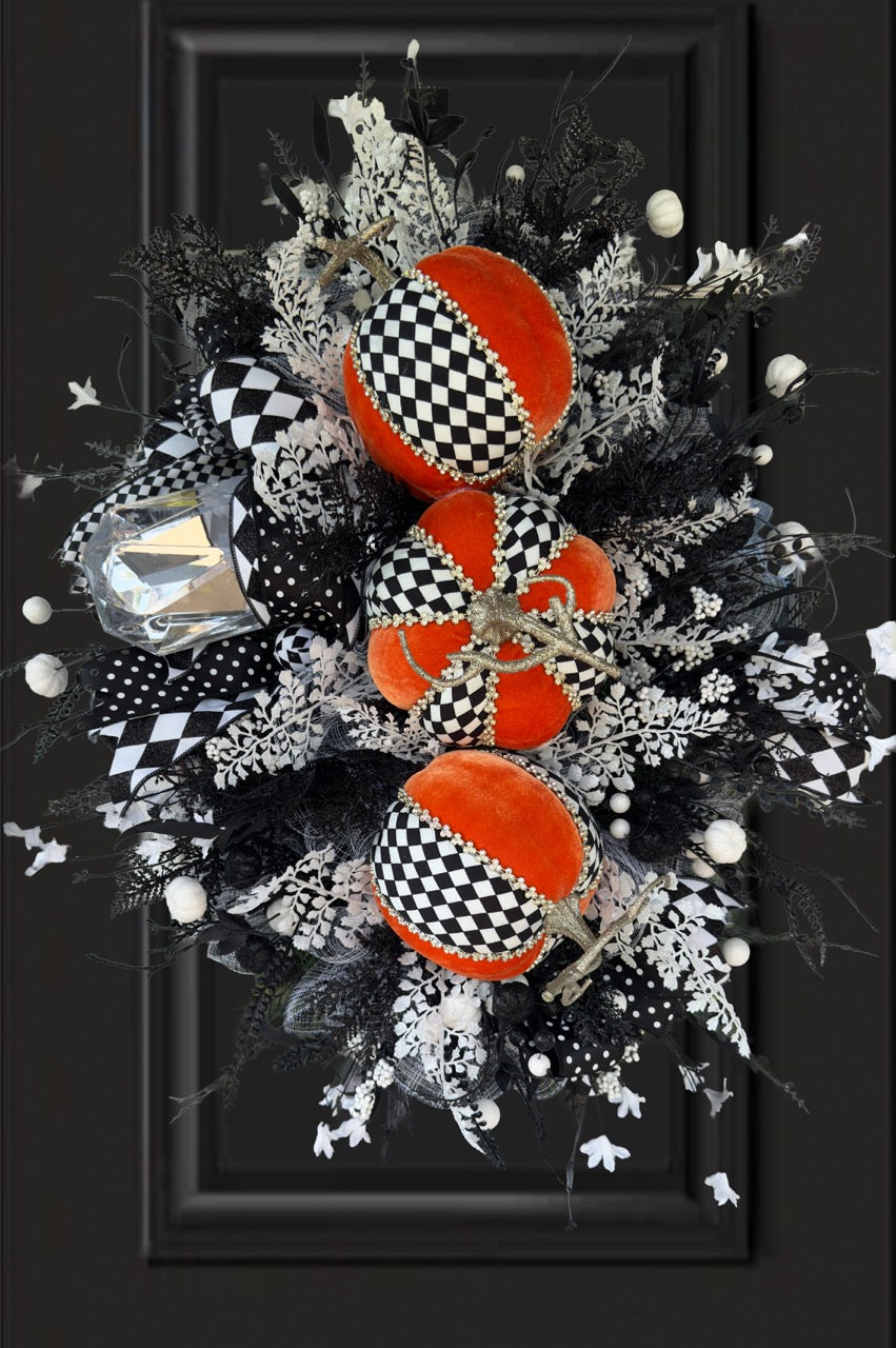 Handmade fall wreath with black‑and‑white checkered pumpkins, gold stems, and black, white, and silver foliage with patterned ribbons on a dark door