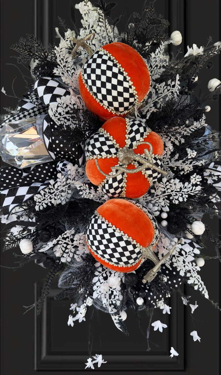 Handmade fall wreath with black‑and‑white checkered pumpkins, gold stems, and black, white, and silver foliage with patterned ribbons on a dark door