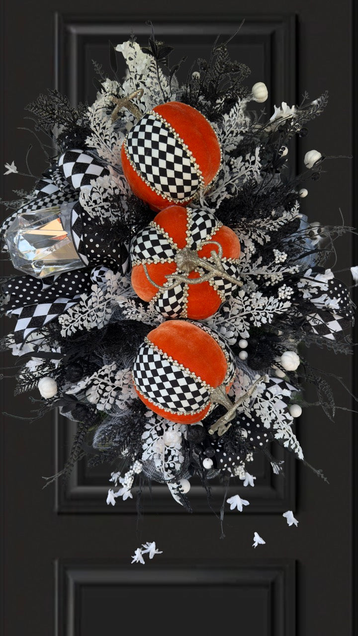 Handmade fall wreath with black‑and‑white checkered pumpkins, gold stems, and black, white, and silver foliage with patterned ribbons on a dark door