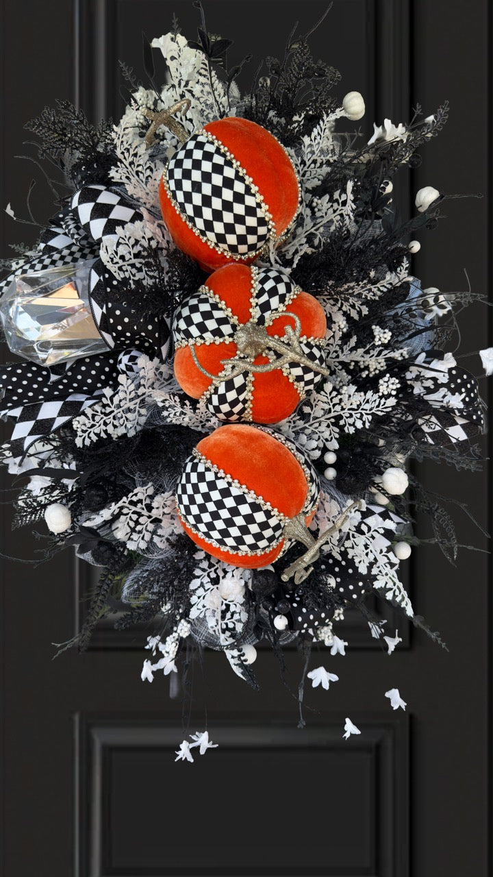 Handmade fall wreath with black‑and‑white checkered pumpkins, gold stems, and black, white, and silver foliage with patterned ribbons on a dark door