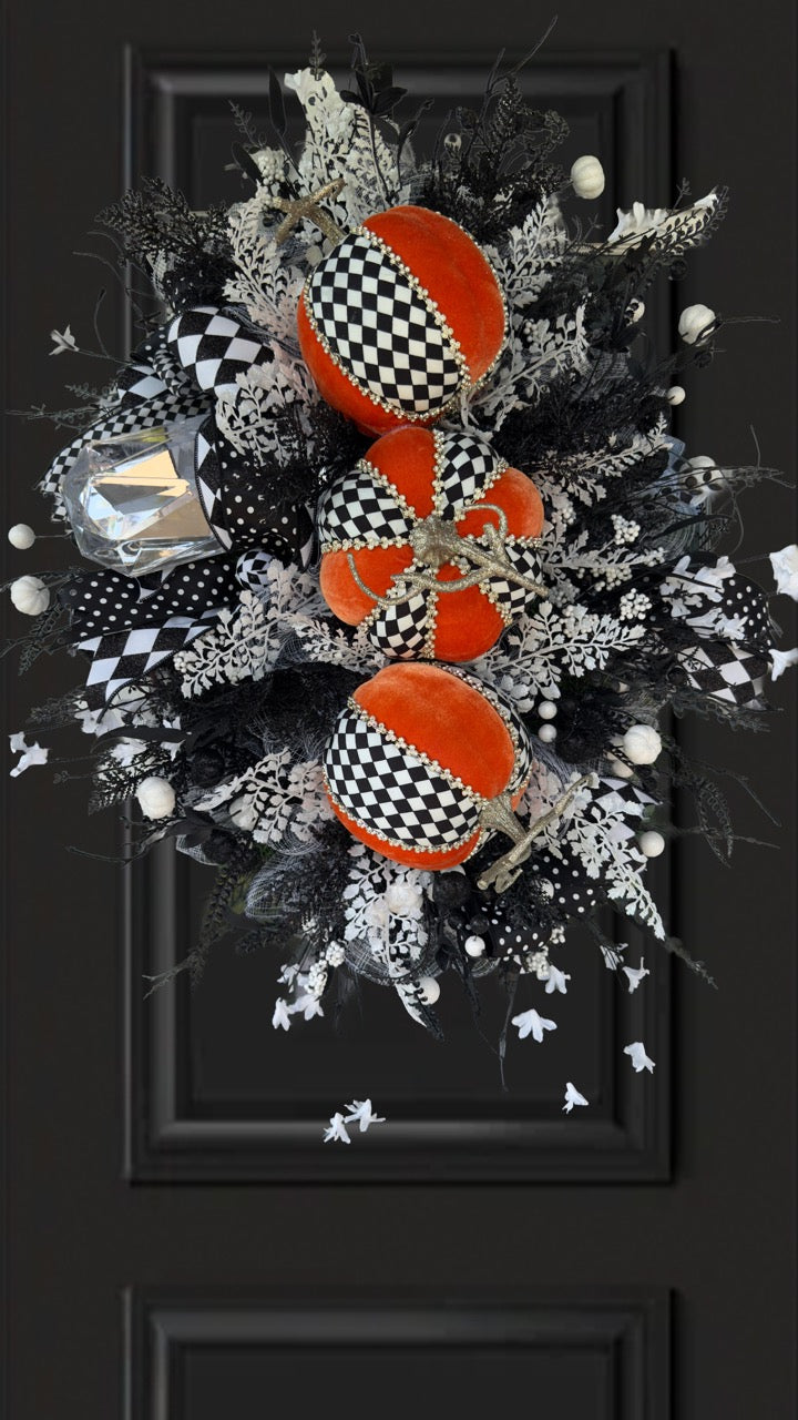 Handmade fall wreath with black‑and‑white checkered pumpkins, gold stems, and black, white, and silver foliage with patterned ribbons on a dark door