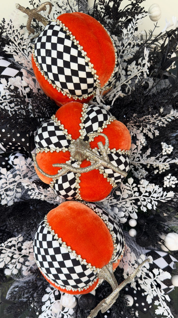 Handmade fall wreath with black‑and‑white checkered pumpkins, gold stems, and black, white, and silver foliage with patterned ribbons on a dark door