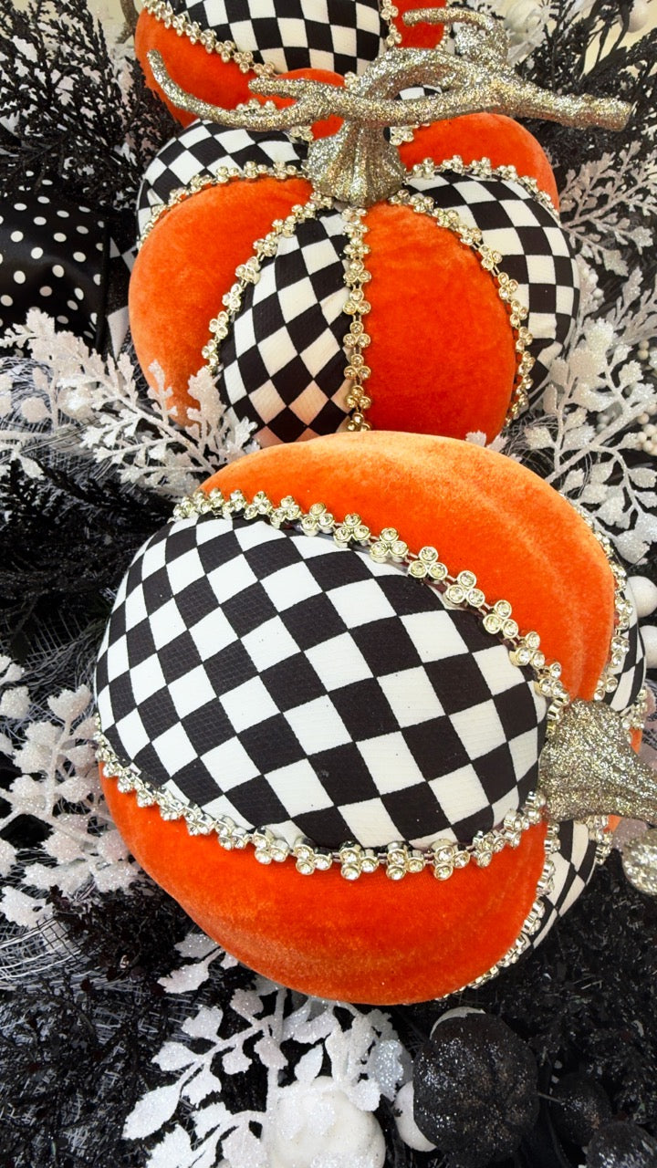 Handmade fall wreath with black‑and‑white checkered pumpkins, gold stems, and black, white, and silver foliage with patterned ribbons on a dark door