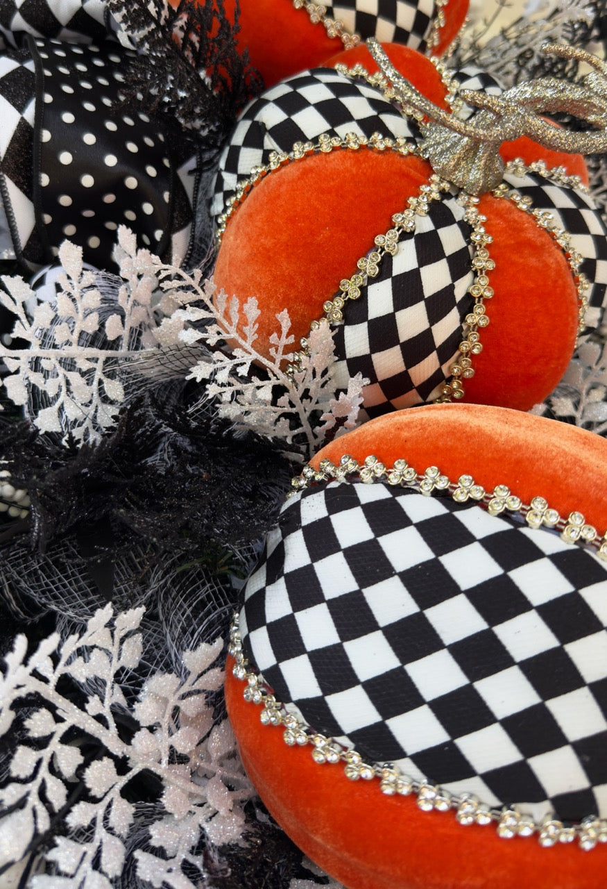 Handmade fall wreath with black‑and‑white checkered pumpkins, gold stems, and black, white, and silver foliage with patterned ribbons on a dark door