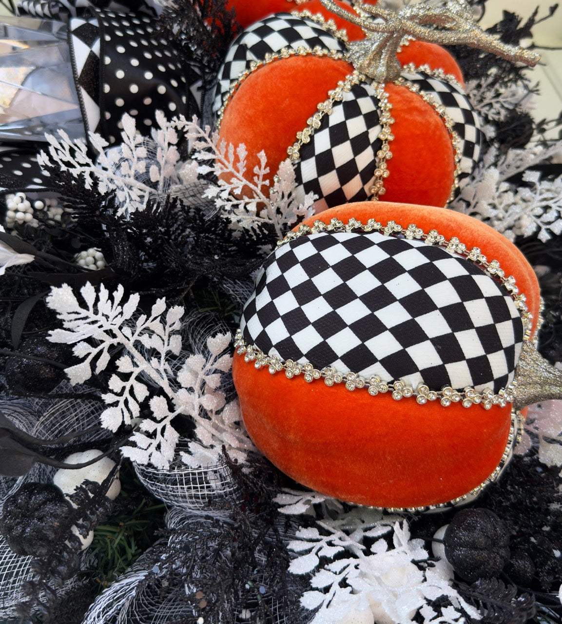 Handmade fall wreath with black‑and‑white checkered pumpkins, gold stems, and black, white, and silver foliage with patterned ribbons on a dark door
