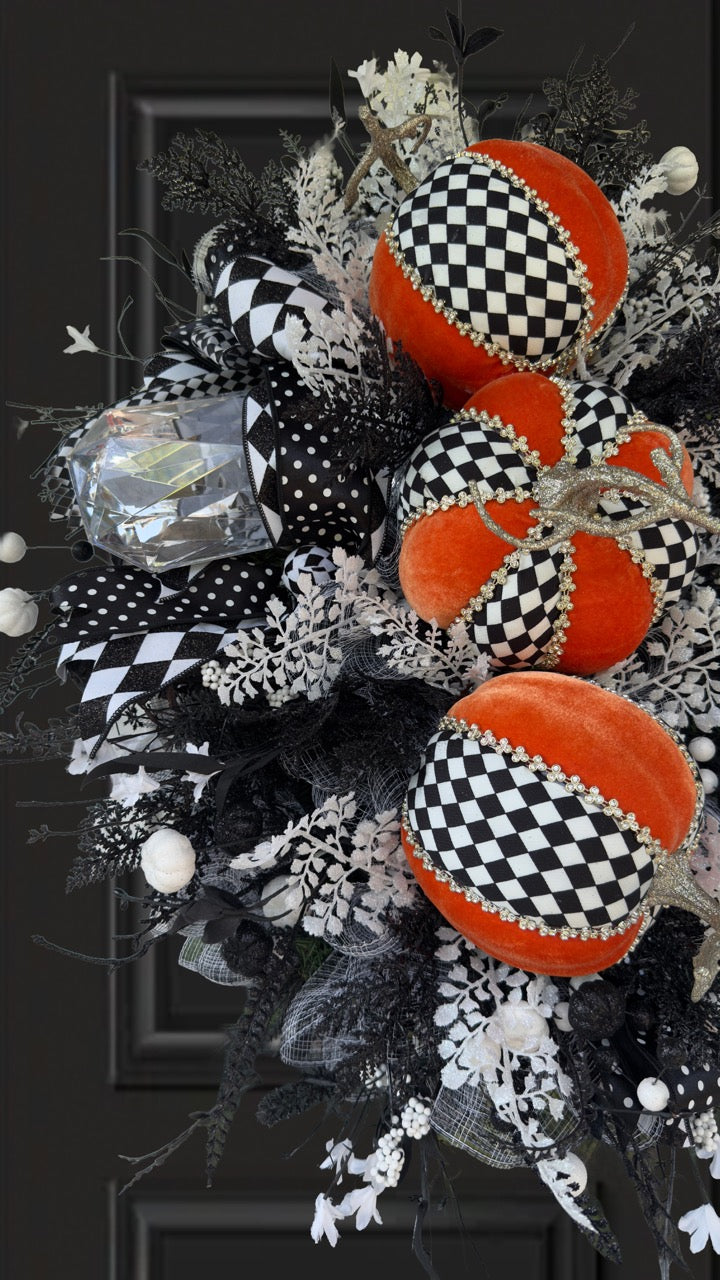 Handmade fall wreath with black‑and‑white checkered pumpkins, gold stems, and black, white, and silver foliage with patterned ribbons on a dark door