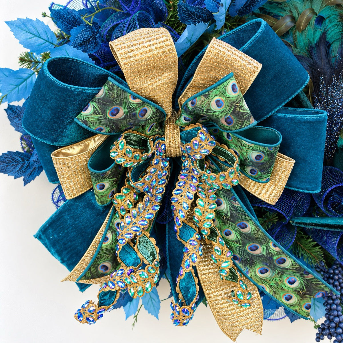 Close-up of luxury peacock wreath bow featuring teal, navy, peacock-patterned ribbon, and gold accents.