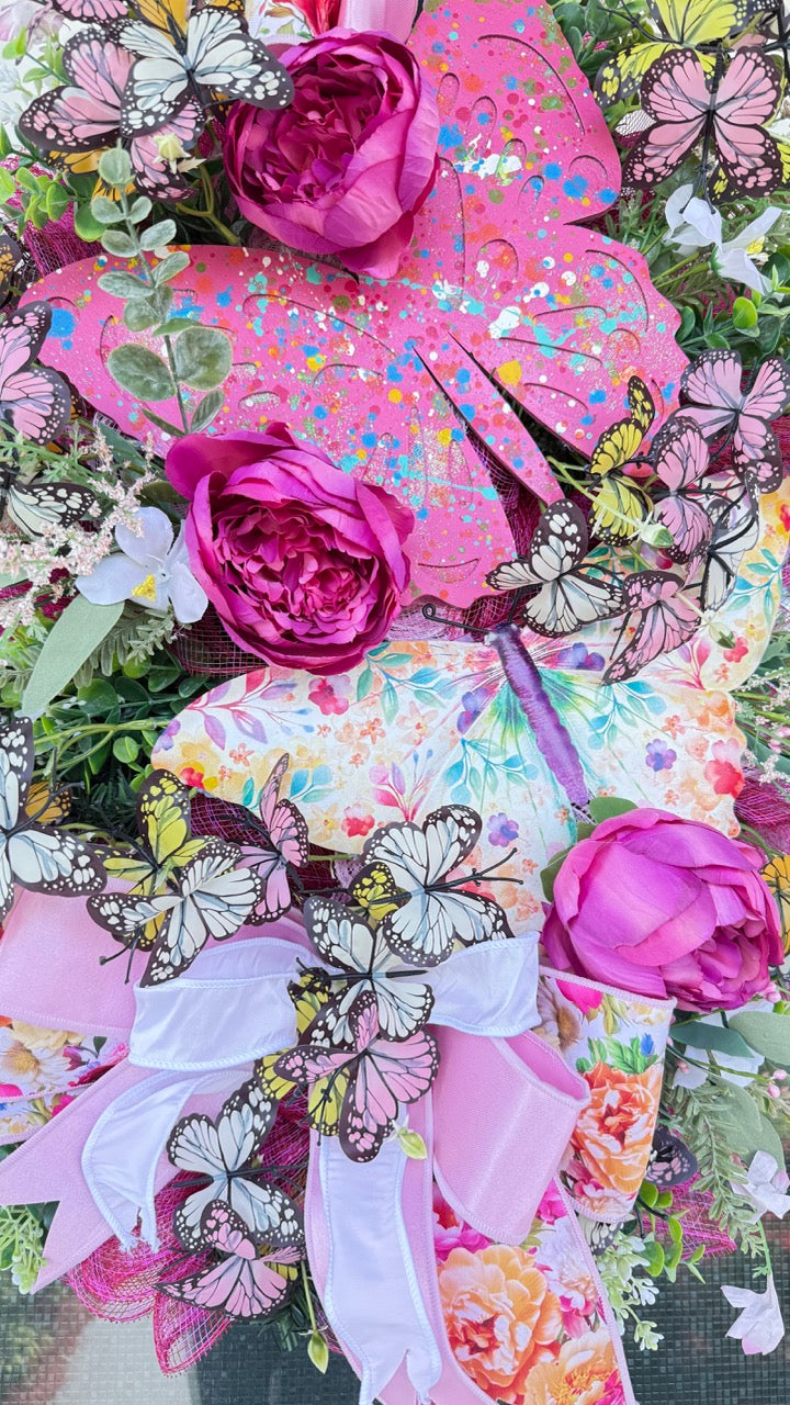 Handmade pink butterfly wreath featuring vibrant florals, layered designer ribbons, lush greenery, and colorful butterflies. This whimsical spring and summer front door wreath creates a beautiful statement piece perfect for entryways, porch decor, and everyday home decorating.