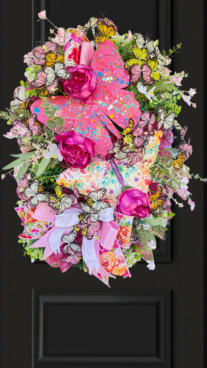 Handmade pink butterfly wreath featuring vibrant florals, layered designer ribbons, lush greenery, and colorful butterflies. This whimsical spring and summer front door wreath creates a beautiful statement piece perfect for entryways, porch decor, and everyday home decorating.