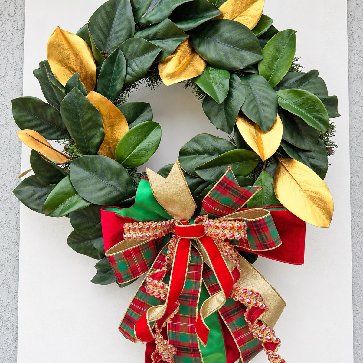 Handmade magnolia Christmas wreath with gold leaves and oversized red green tartan plaid and jeweled holiday bow