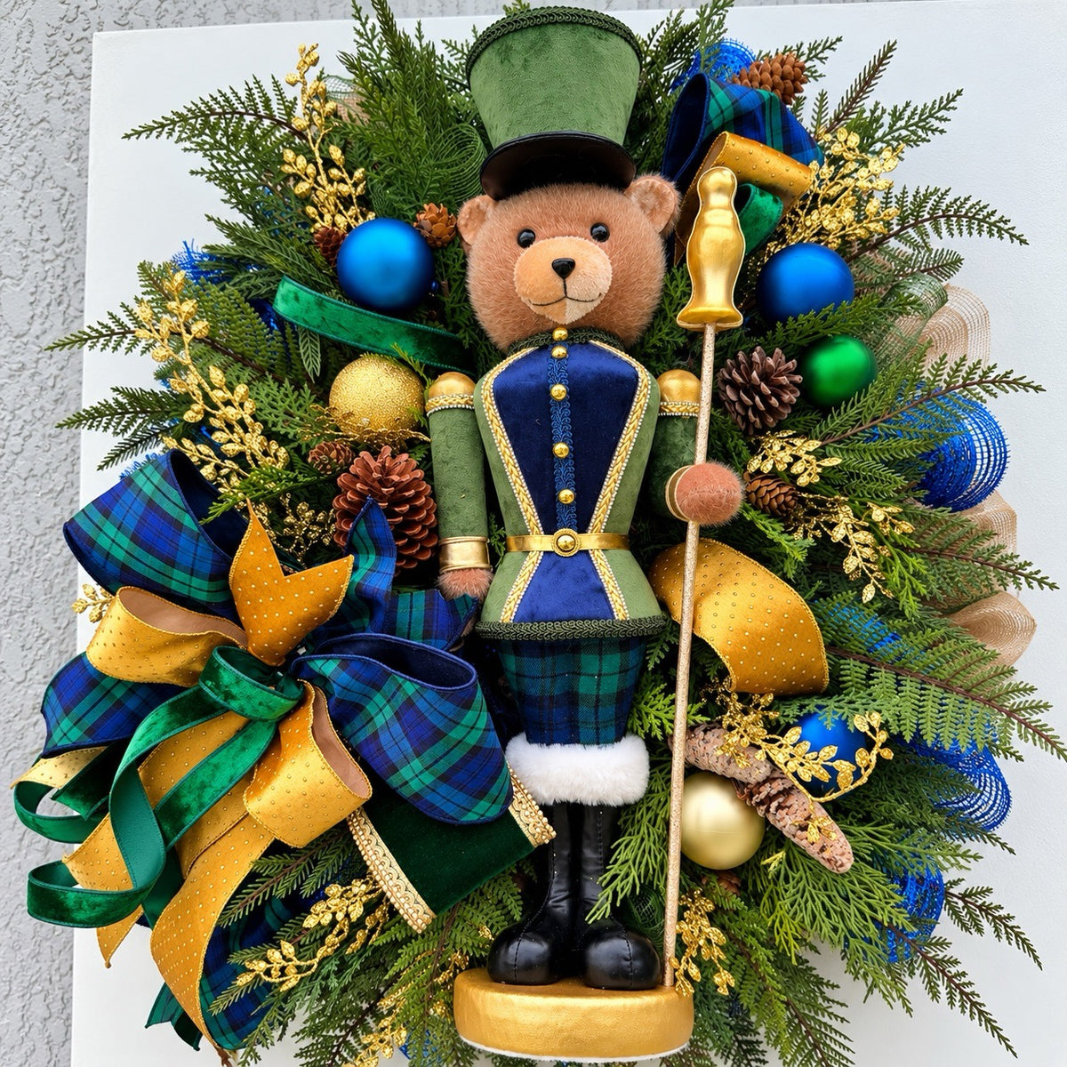 Full view of handmade teddy bear Christmas wreath with evergreen, navy ornaments and gold ribbon.