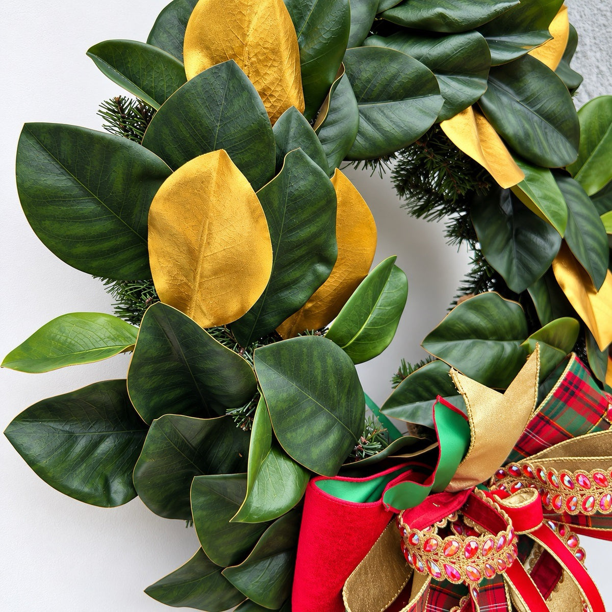 Handmade magnolia Christmas wreath with gold leaves and oversized red green tartan plaid and jeweled holiday bow