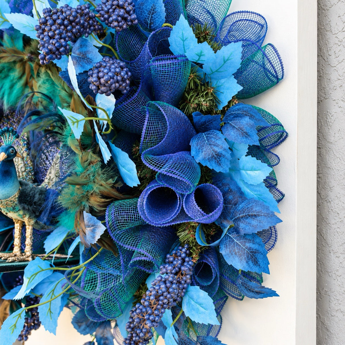 Detailed view of decorative blue leaves and berry clusters on a handmade peacock wreath.