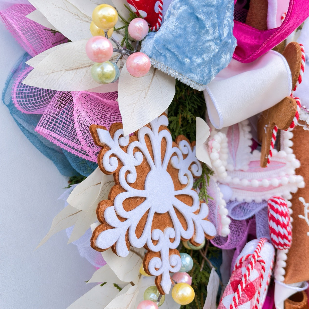 Sugarplum Gingerbread Cottage Christmas Wreath with pastel gingerbread house, pink and blue bows, poinsettias and Norfolk fir greenery.