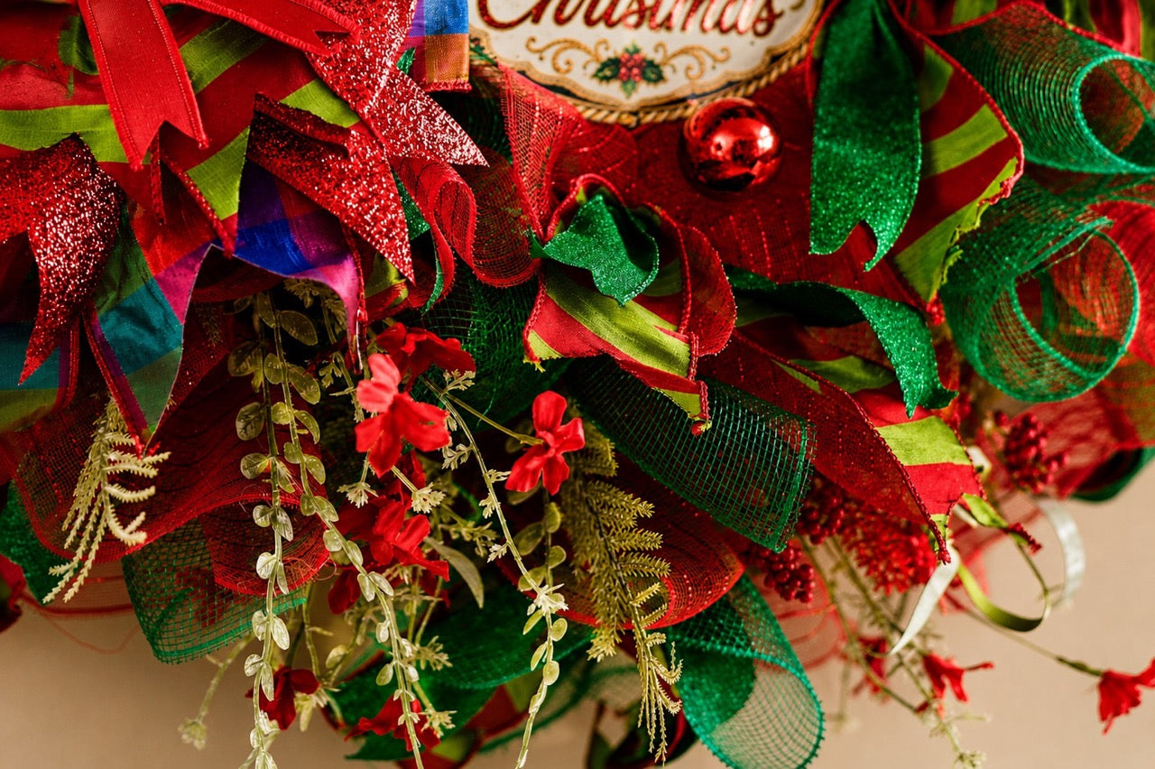 Handcrafted red and emerald green Nutcracker Christmas wreath with Merry Christmas centerpiece, glitter ribbon, ornaments, berries, mesh, and gold accents.