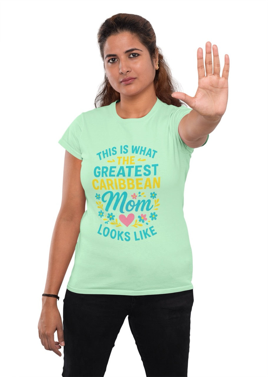 Woman wearing a green T-shirt with colorful text reading “This is what the greatest Caribbean mom looks like,” decorated with flowers and a heart, raising her hand in a stop gesture.