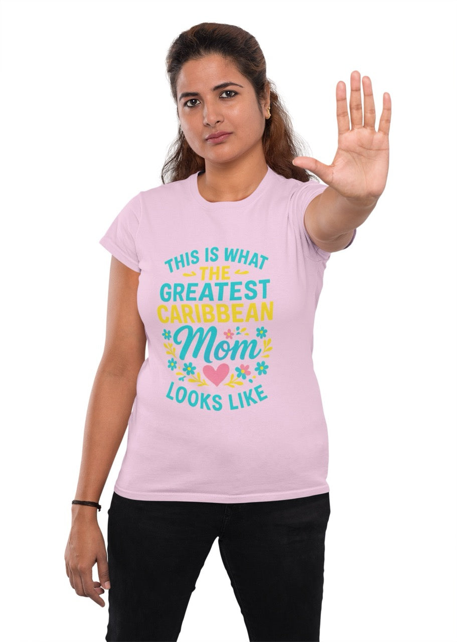 Woman wearing a pink T-shirt with colorful text reading “This is what the greatest Caribbean mom looks like,” decorated with flowers and a heart, raising her hand in a stop gesture.