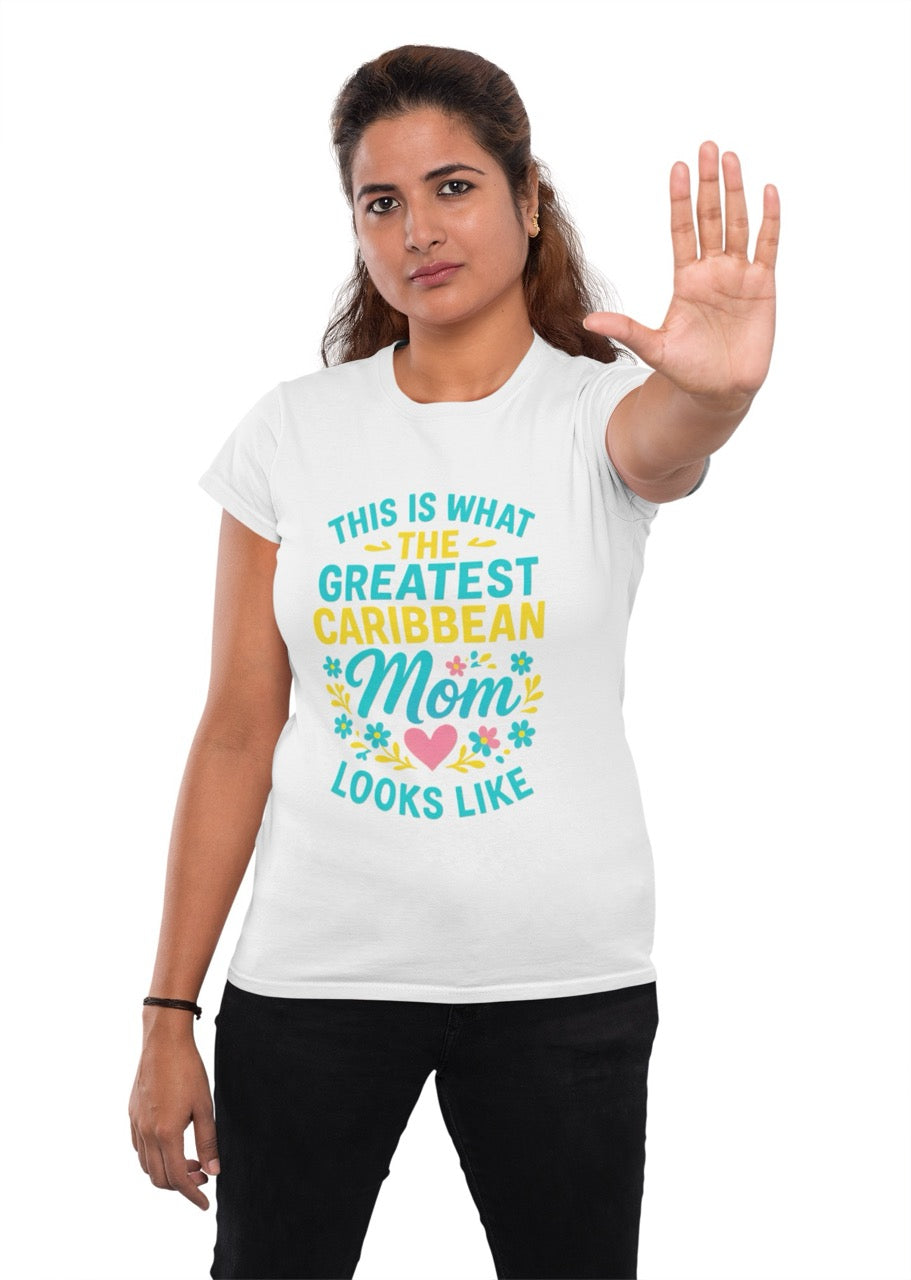 Woman wearing a white T-shirt with colorful text reading “This is what the greatest Caribbean mom looks like,” decorated with flowers and a heart, raising her hand in a stop gesture.