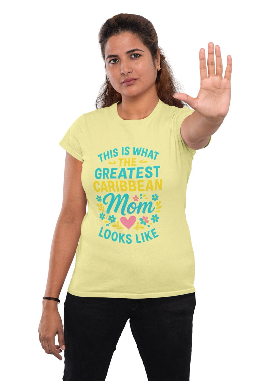 Woman wearing a light yellow T-shirt with colorful text reading “This is what the greatest Caribbean mom looks like,” decorated with flowers and a heart, raising her hand in a stop gesture.