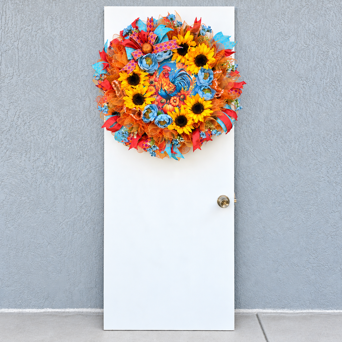 Handmade fall rooster wreath featuring vibrant yellow sunflowers, dusty blue flowers, orange deco mesh, coral and turquoise ribbons, and a colorful rooster centerpiece. A full farmhouse-style autumn wreath displayed on a white front door.