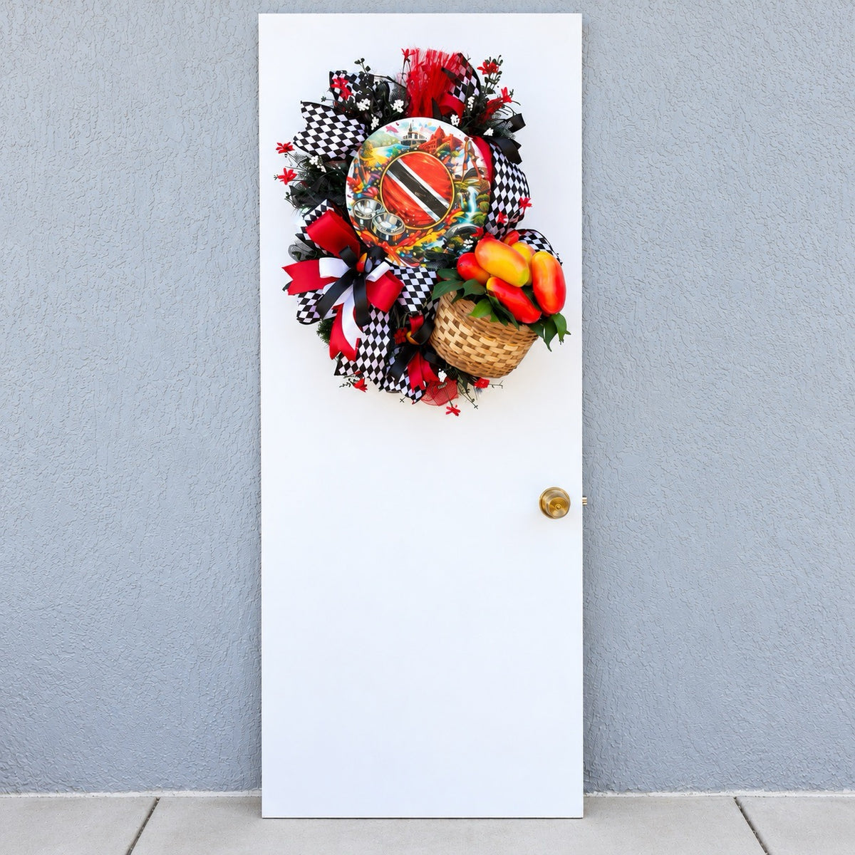 Trinidad and Tobago Caribbean wreath displayed on a white front door with bold red black and white ribbons, tropical greenery, decorative pepper basket and Trinidad flag centerpiece.
