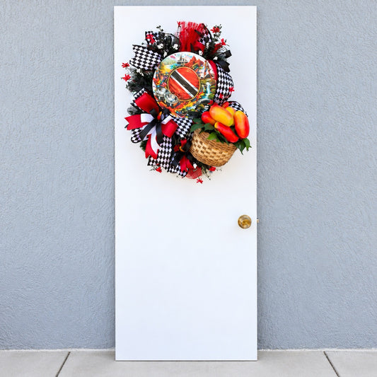 Trinidad and Tobago Caribbean wreath displayed on a white front door with bold red black and white ribbons, tropical greenery, decorative pepper basket and Trinidad flag centerpiece.