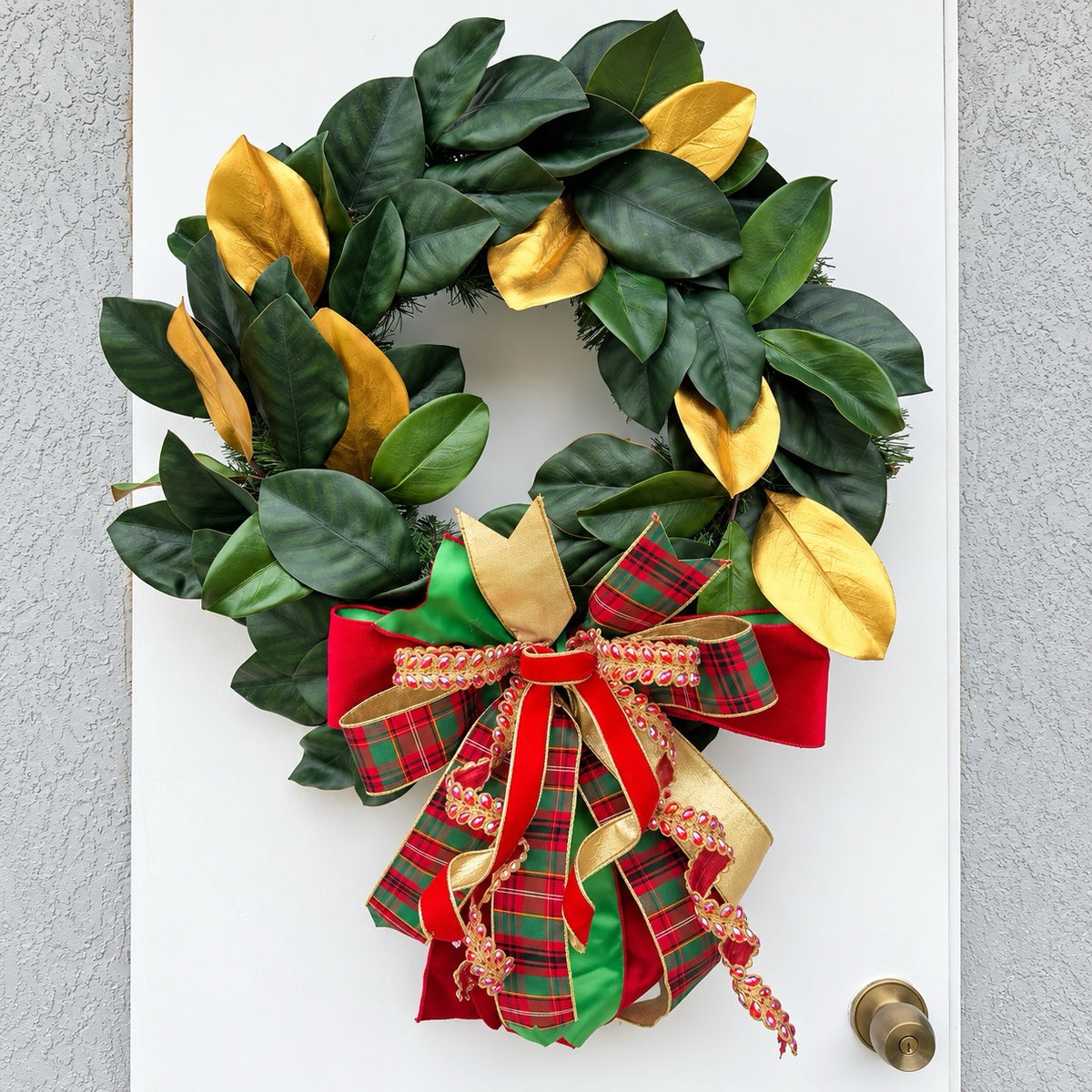 Handmade magnolia Christmas wreath with gold leaves and oversized red green tartan plaid and jeweled holiday bow