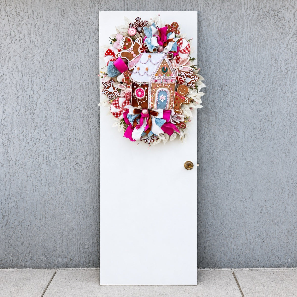Sugarplum Gingerbread Cottage Christmas Wreath with pastel gingerbread house, pink and blue bows, poinsettias and Norfolk fir greenery.