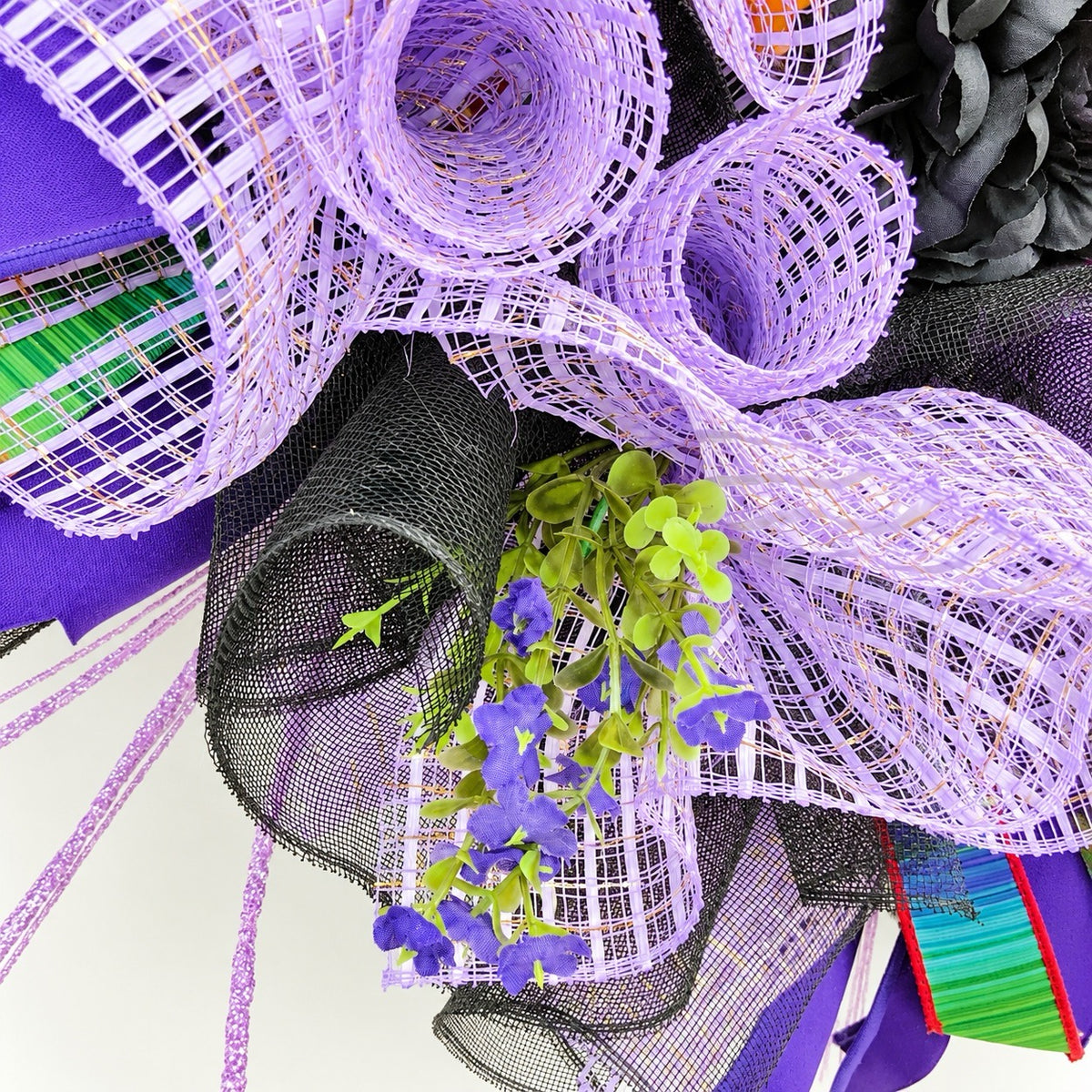 Close-up of purple florals, greenery, glitter accents and layered mesh on Halloween wreath