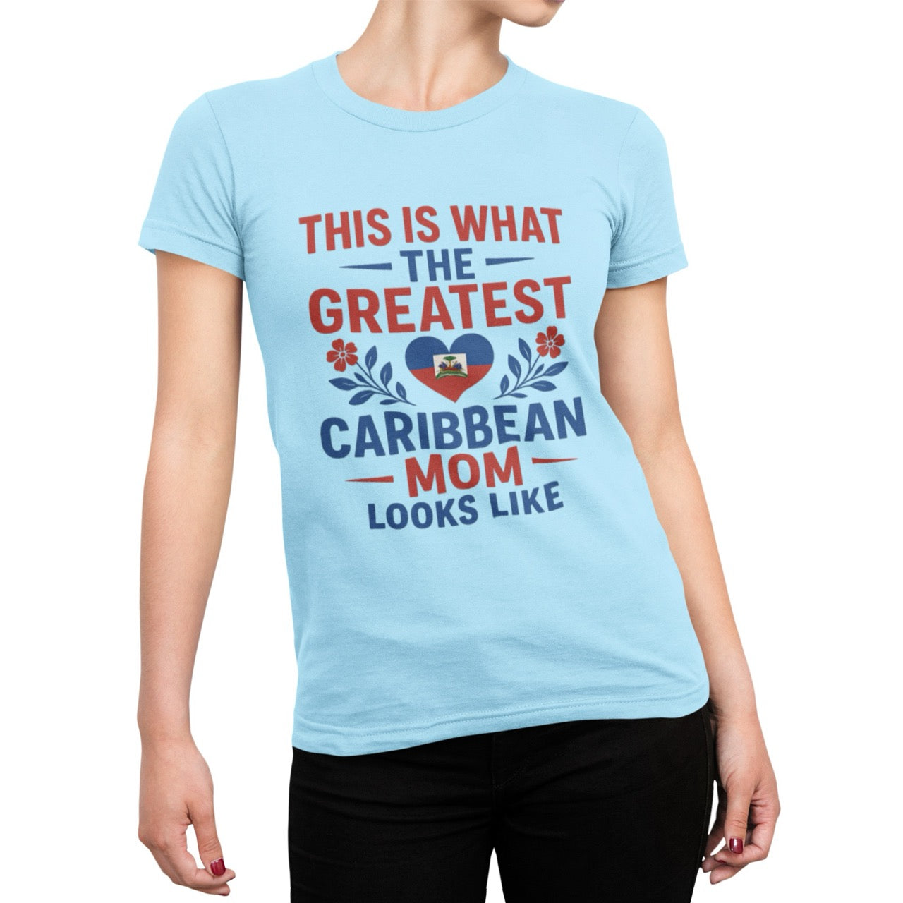 Woman wearing a pink T-shirt with bold red and blue text reading “This is what the greatest Caribbean mom looks like,” featuring a heart with the Haitian flag and floral accents.