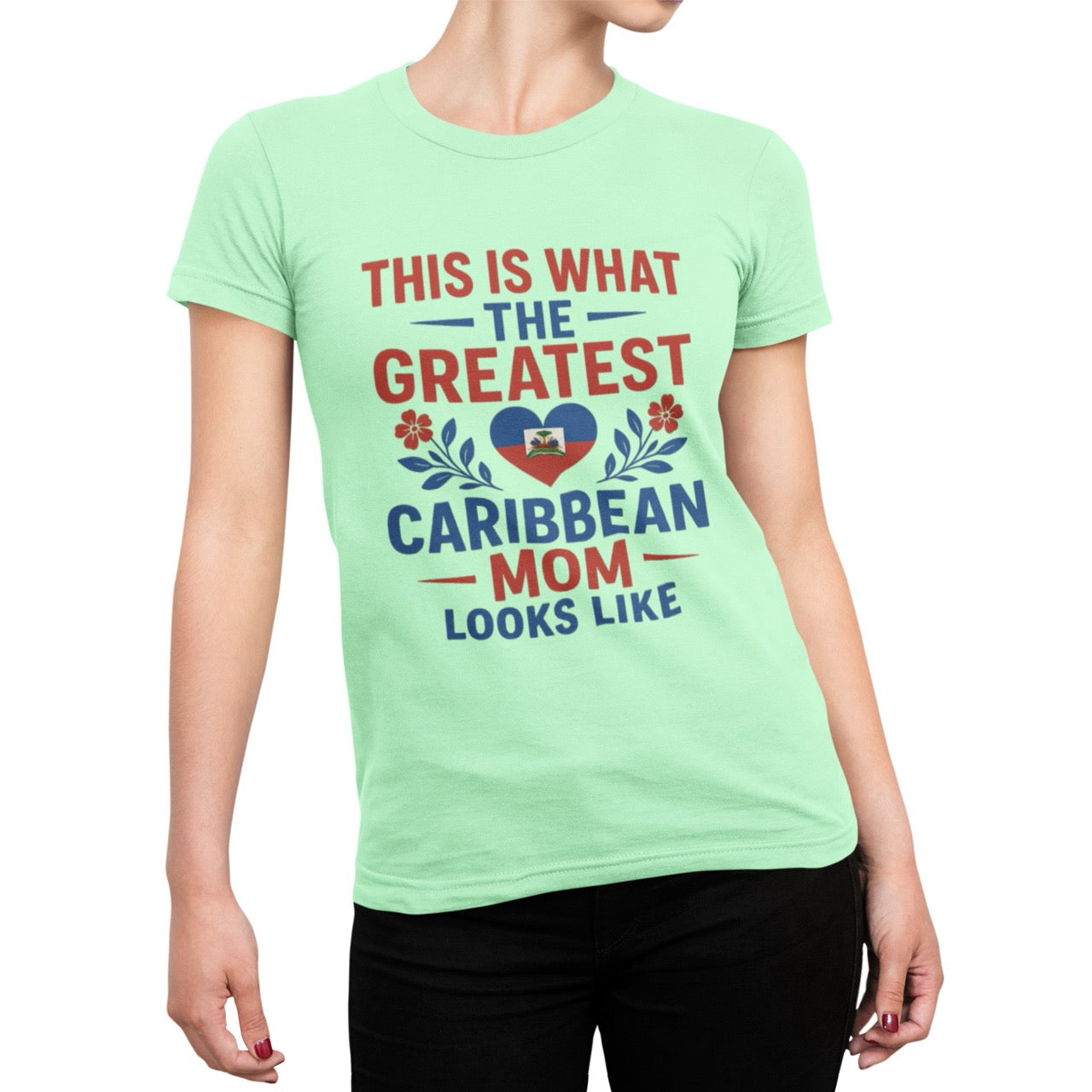 Woman wearing a pink T-shirt with bold red and blue text reading “This is what the greatest Caribbean mom looks like,” featuring a heart with the Haitian flag and floral accents.