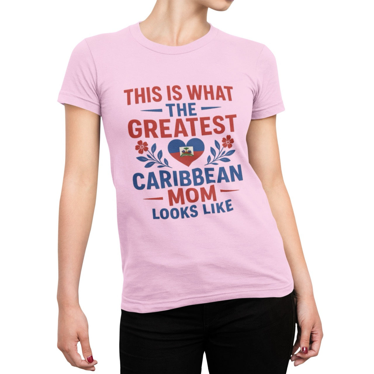 Woman wearing a pink T-shirt with bold red and blue text reading “This is what the greatest Caribbean mom looks like,” featuring a heart with the Haitian flag and floral accents.