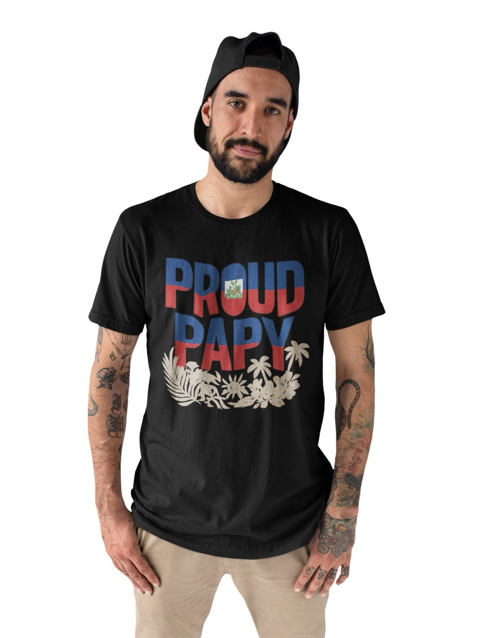 Man wearing a black T-shirt with bold text reading “Proud Papy,” featuring Haitian flag colors and tropical floral accents.