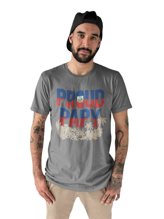 Man wearing a gray T-shirt with bold text reading “Proud Papy,” featuring Haitian flag colors and tropical floral accents.