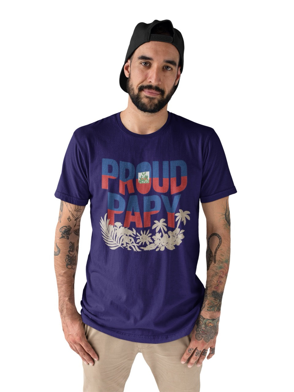 Man wearing a purple T-shirt with bold text reading “Proud Papy,” featuring Haitian flag colors and tropical floral accents.