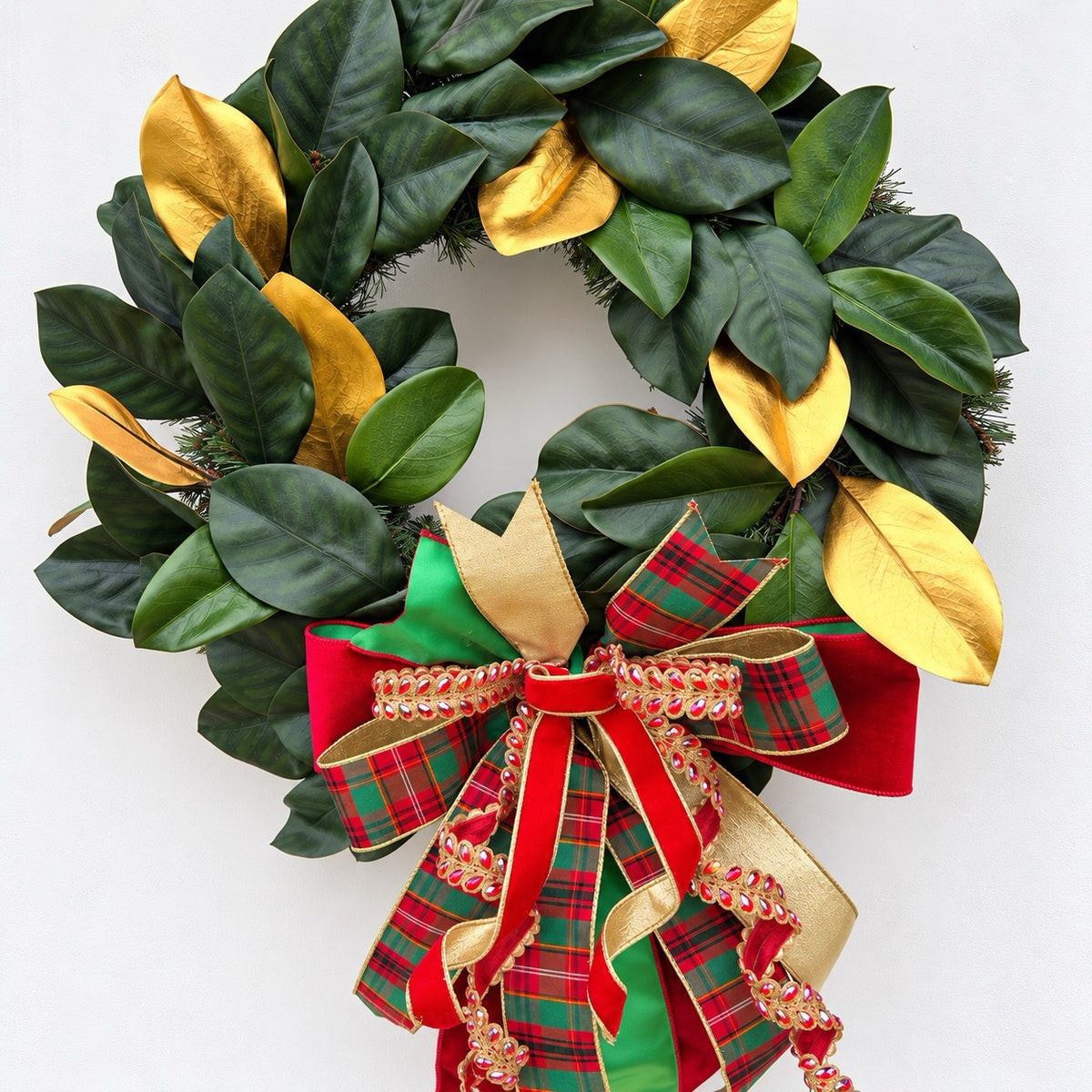 Handmade magnolia Christmas wreath with gold leaves and oversized red green tartan plaid and jeweled holiday bow