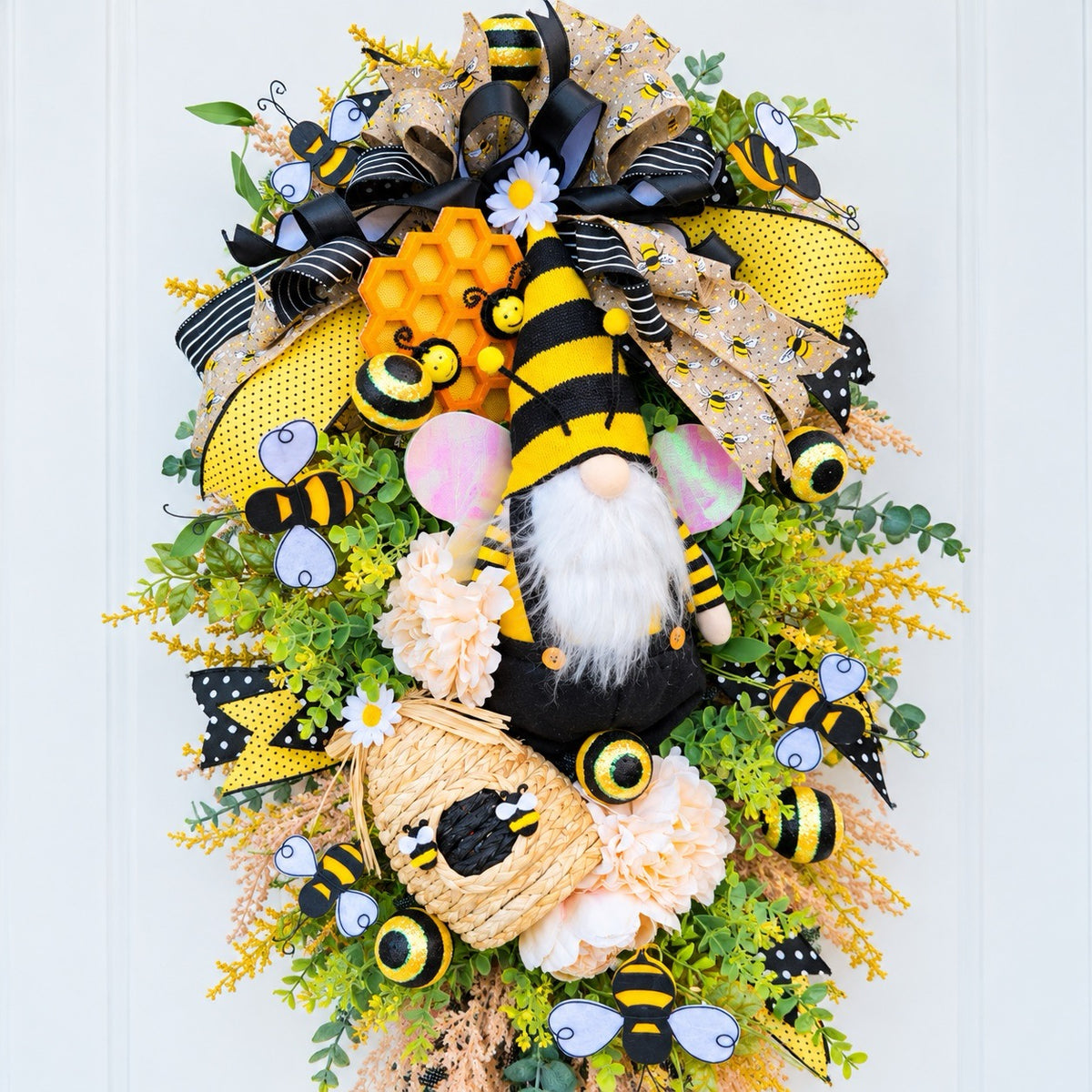 Handmade Queen Bee Manor wreath featuring a bee gnome, woven beehive, yellow and black designer bow, honeycomb accents, florals, bees, and lush greenery.