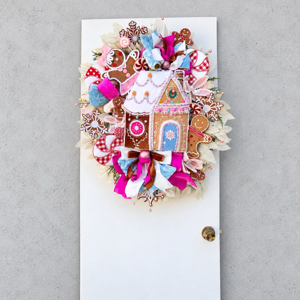 Sugarplum Gingerbread Cottage Christmas Wreath with pastel gingerbread house, pink and blue bows, poinsettias and Norfolk fir greenery.