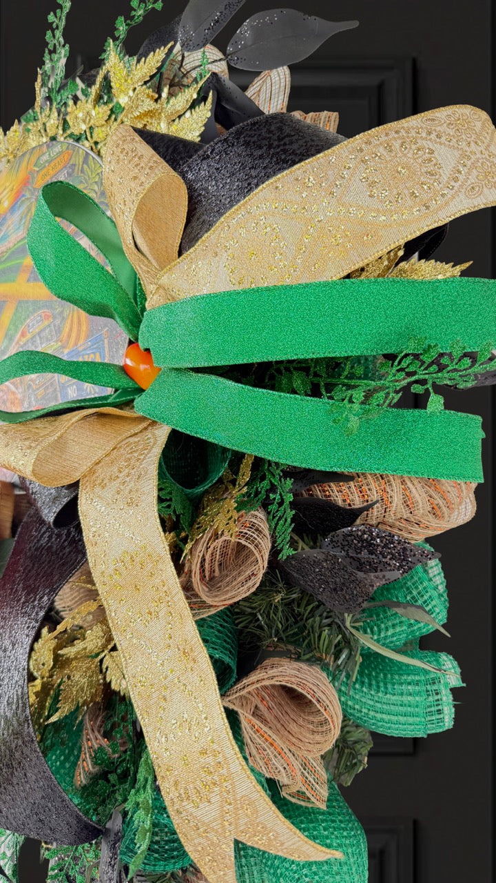 Luxury handmade Jamaica-inspired door wreath featuring green, black, and gold designer ribbons, tropical fruit basket, glittered foliage, and colorful island-themed artwork celebrating Jamaican culture and Caribbean décor.
